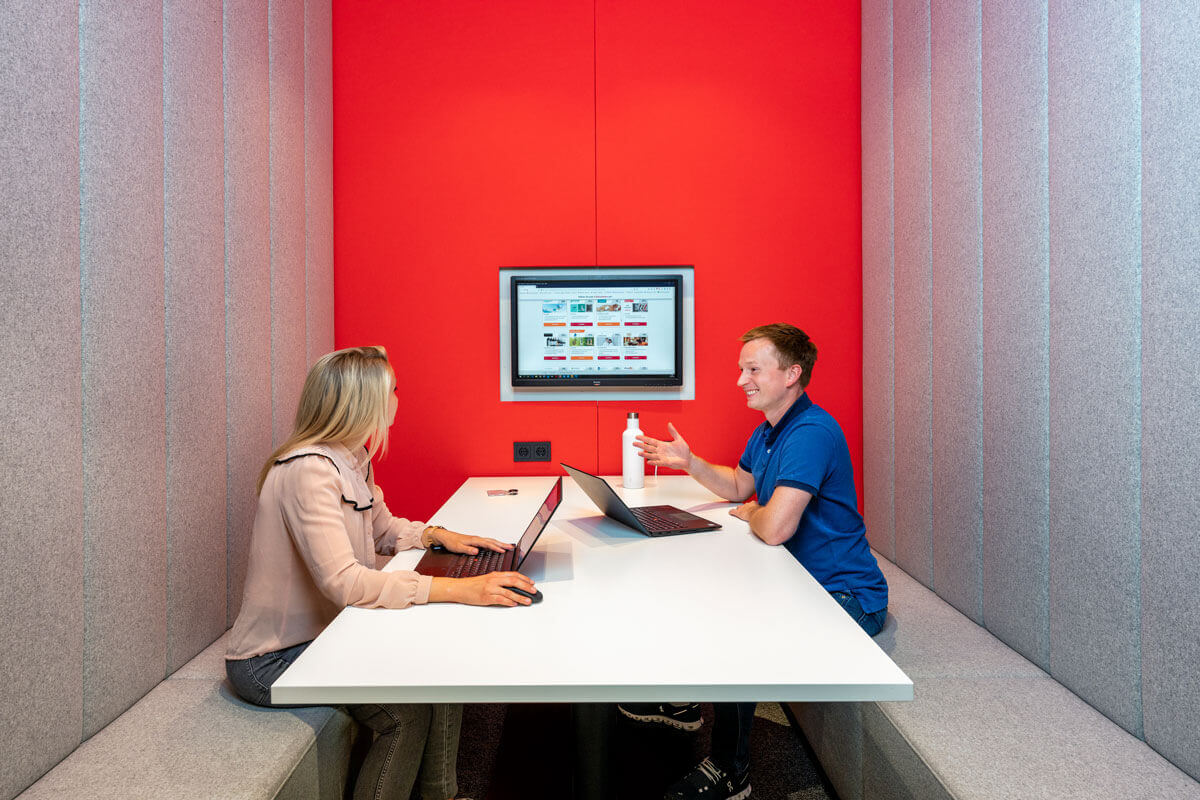 Das Team von voucher Products bei einem Gespräch in einem Meetingraum. Beide haben einen Laptop vor sich stehen und unterhalten sich angeregt. Im Hintergrund ist ein Bildschirm mit der Gutscheinauswahlseite zu sehen.